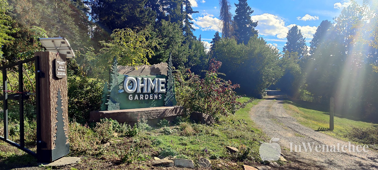 The Ohme Gardens entrance sign beside a stone gate pillar and a gravel path.