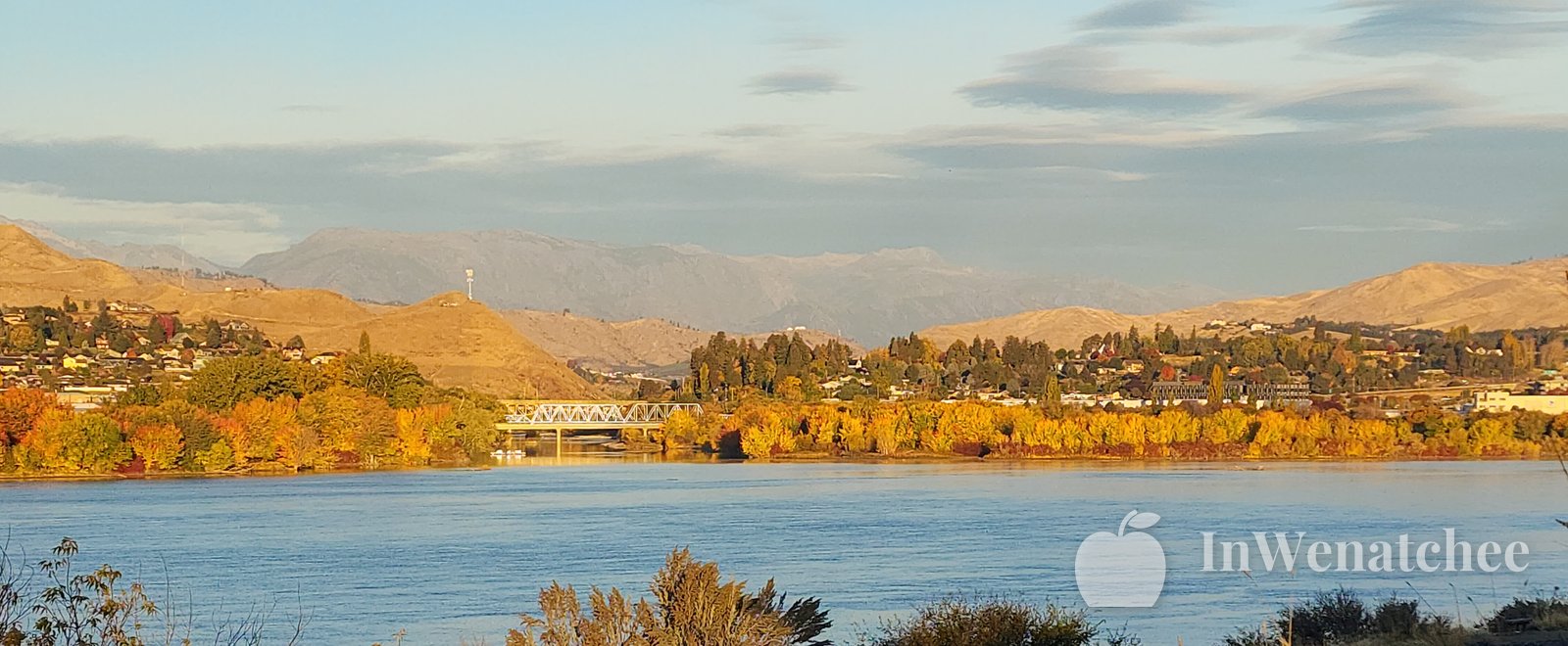 Fall color along the Columbia at the Wenatchee riverfront, with yellow and orange trees across the far bank and blue water in the foreground.