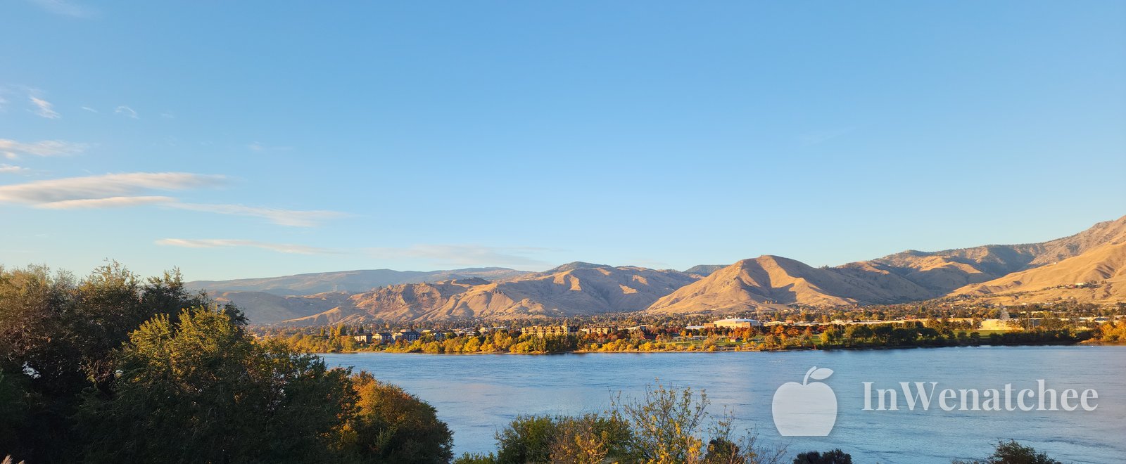 Sun flare along a trail through sagebrush, with dry shrubs in the foreground and bright sky over the Wenatchee hills.
