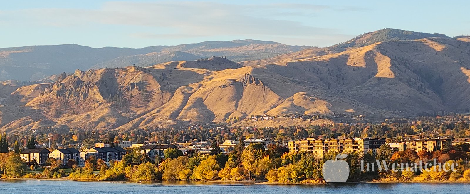 Autumn trees in yellow and orange along the Columbia, with the Wenatchee hills under a bright sky and a narrow band of river.
