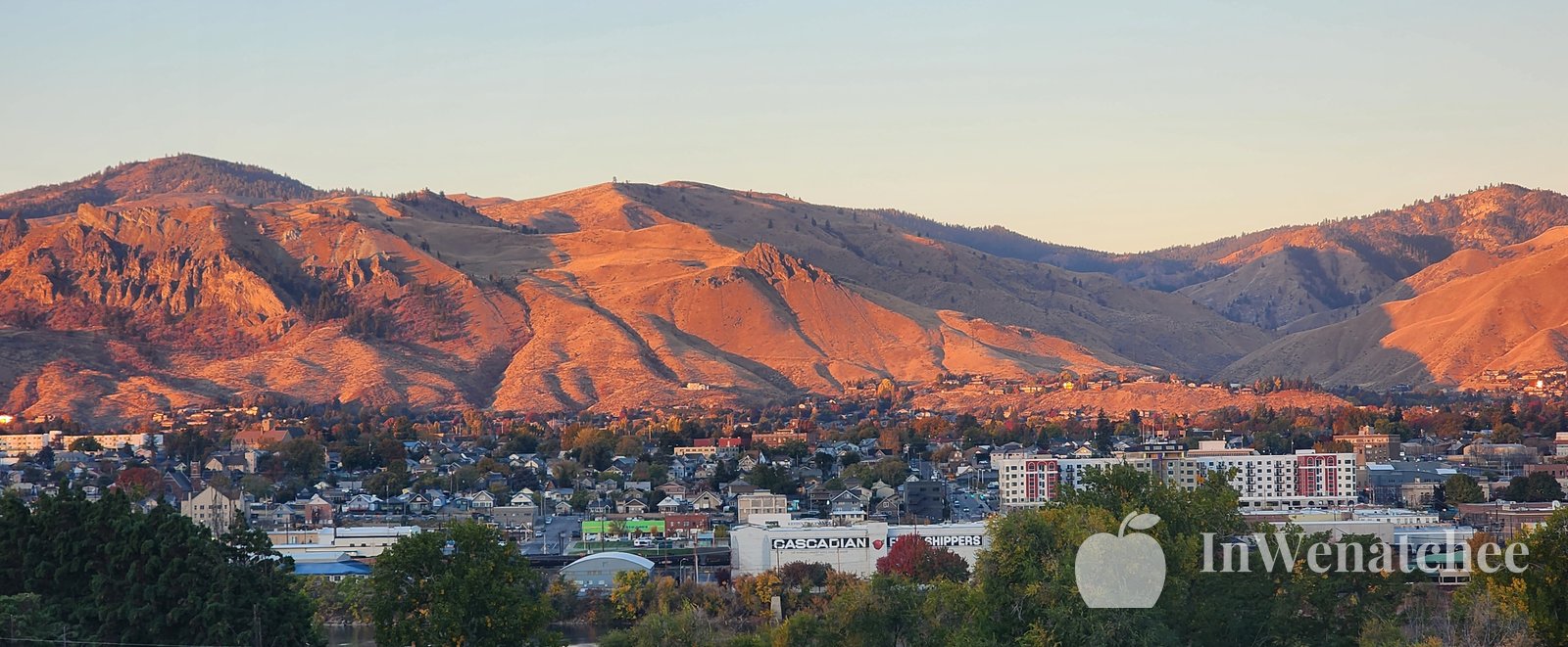 Mountains behind downtown Wenatchee, with the city along the Columbia River and a bridge crossing the water.